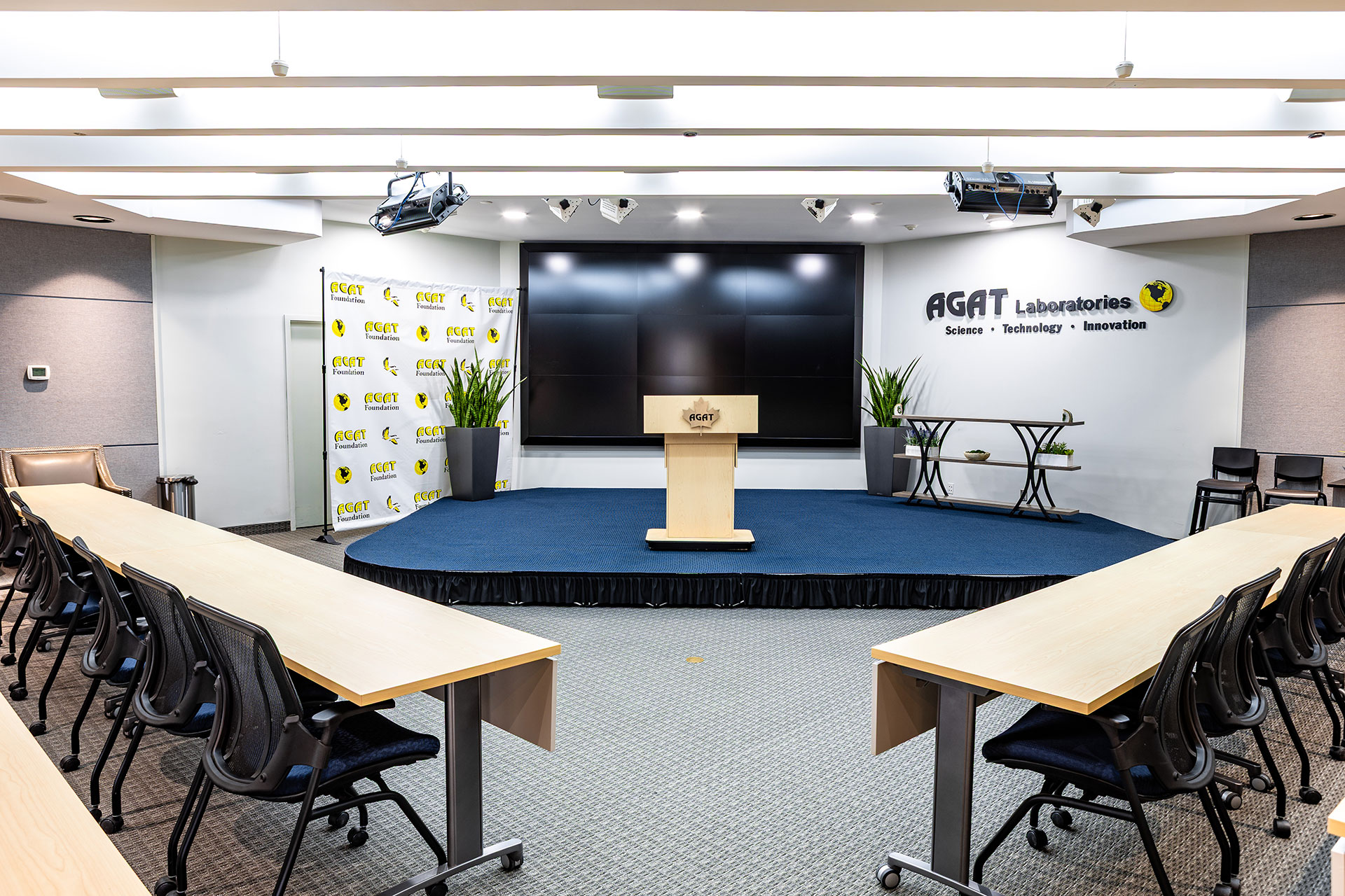 Wide view of the Michael DeSanti Centre for Excellence auditorium with podium, stage, and video wall.