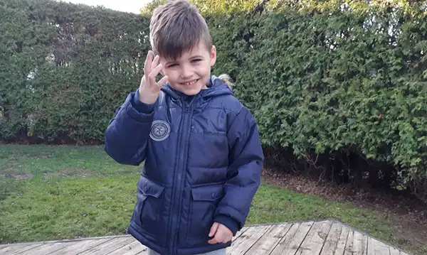 Young boy in blue coat smiling and waving, symbolizing hope and strength in the face of POLG disease.